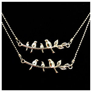 a picture of two necklaces on a velvet background. One is a branch with three birds. The other is a branch with four birds. Both necklaces are silver tone metal.